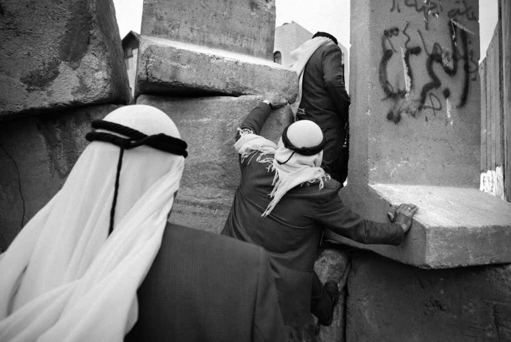 Palestinian men climb over an unfinished section of Israel's separation barrier - בלילטי עודד
