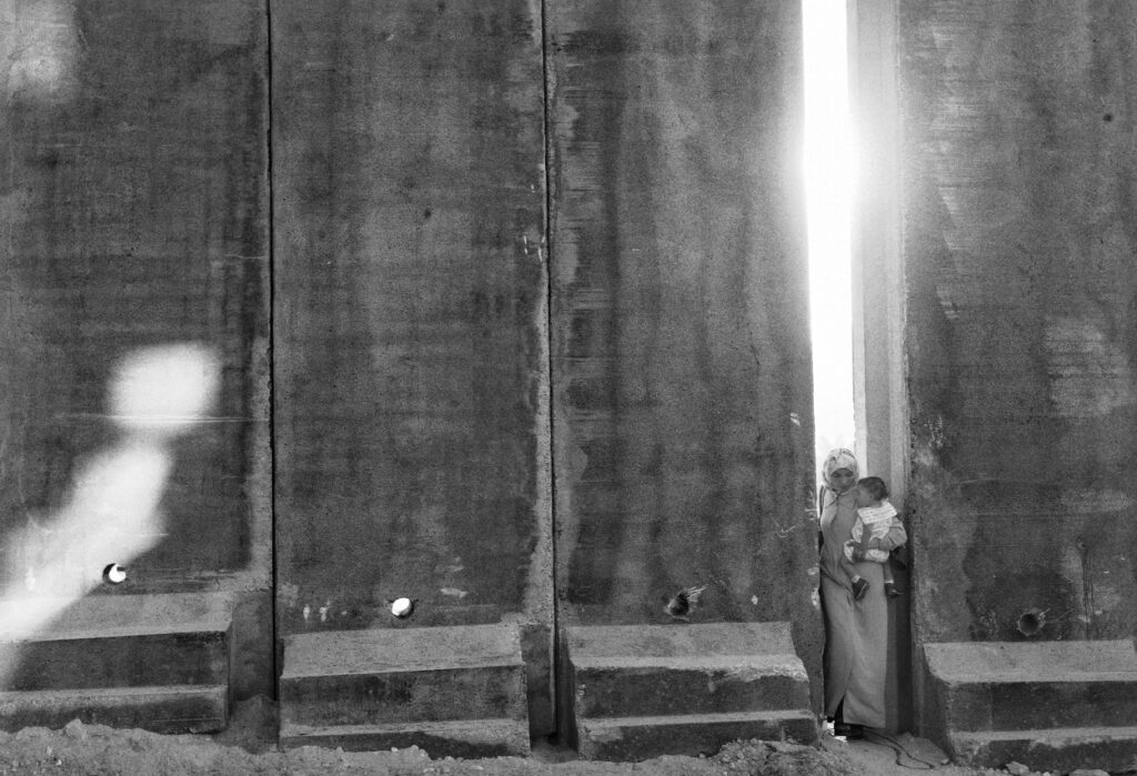 A Palestinian woman holding a baby cross through a gap in a section of the 8-meter-high wall - בלילטי עודד